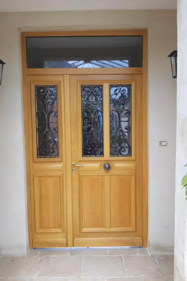Porte d'entrée chêne clair, imposte arquée, ferronnerie noire et mur crépi beige