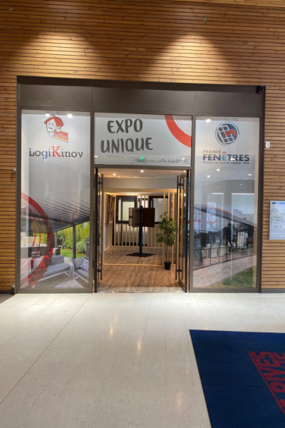 Entrée showroom EXPO UNIQUE avec logos France Fenêtres et mascotte sur vitrine décorée