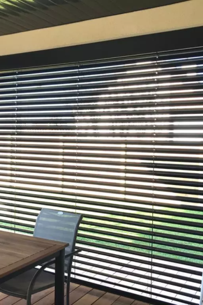 Brise-soleil orientable anthracite incliné au-dessus d'une terrasse bois, table et fauteuil gris