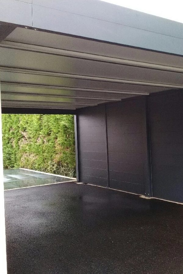 Intérieur carport anthracite toit lambris, panneaux lateraux opaques, haie verte au fond