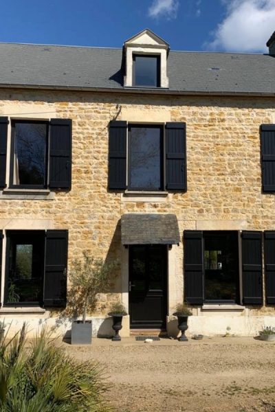 Maison pierre rénovée, fenêtres et porte noires, volets battants noirs et lucarne