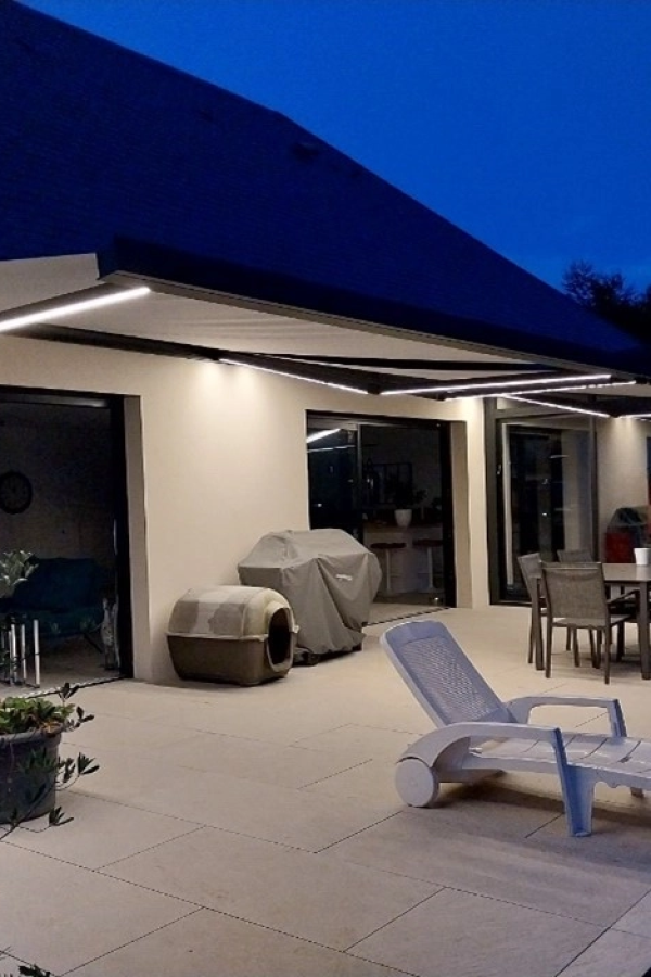 Store banne déployé la nuit avec éclairage LED intégré sur terrasse carrelée et transat blanc