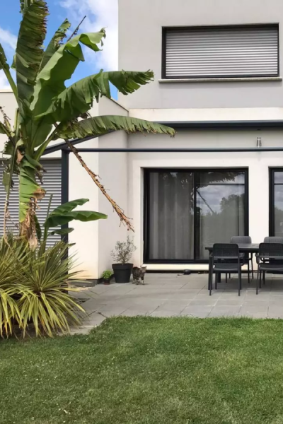Maison claire avec baies noires, volet roulant gris à l'étage, terrasse carrelée et bananier