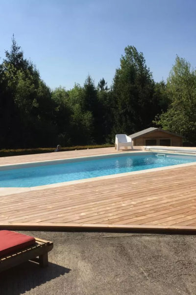 Piscine rectangulaire bleue encastrée dans grande terrasse bois, jardin boisé et cabane