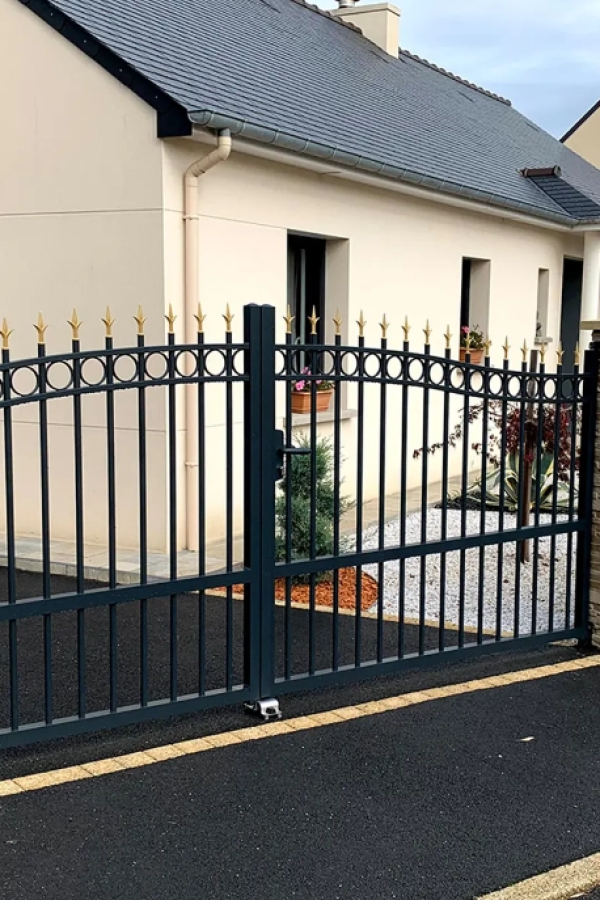 Portail battant noir à barreaux avec finitions dorées devant maison beige toit ardoise