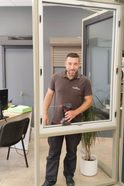 Technicien souriant avec perceuse Bosch devant châssis fenêtre beige en showroom