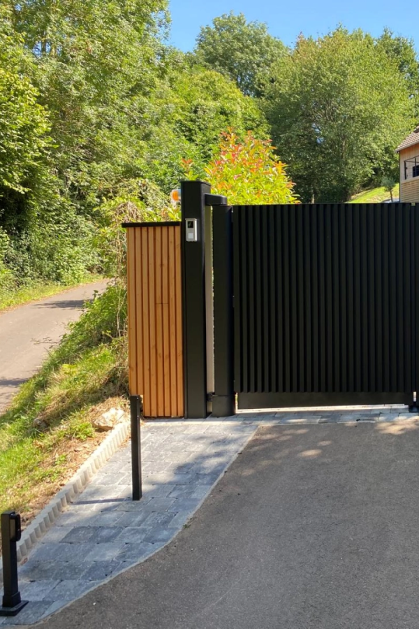 Portail battant noir lames verticales avec poteau interphone et clôture bois clair