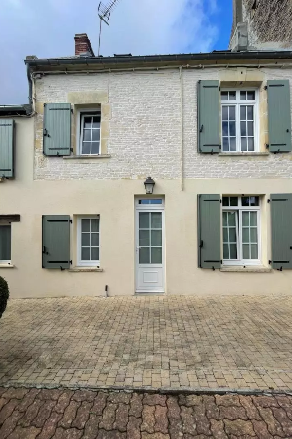 Façade deux niveaux, fenêtres blanches et volets battants vert sauge sur cour pavée
