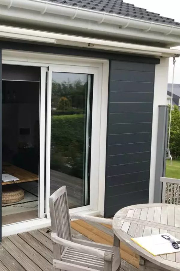 Baie coulissante blanche et panneau occultant anthracite sur terrasse bois, mobilier de jardin