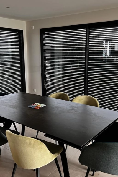 Salle à manger avec table noire, chaises moutarde et brise-soleil orientables noirs