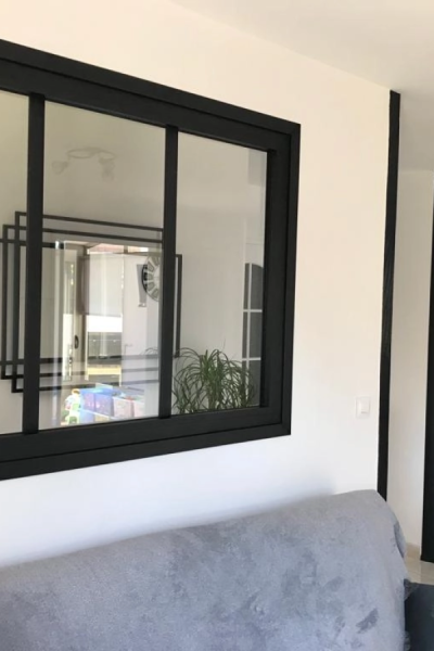 Verrière intérieure cadre noir trois vitrages au-dessus d'un canapé gris sur mur blanc
