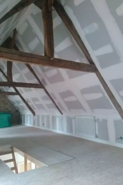 Combles en travaux, murs placo joints visibles, poutres bois, trémie échelle et radiateur