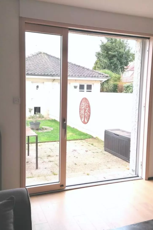 Baie coulissante bois clair ouvrant sur jardin, parquet et canapé gris dans le salon