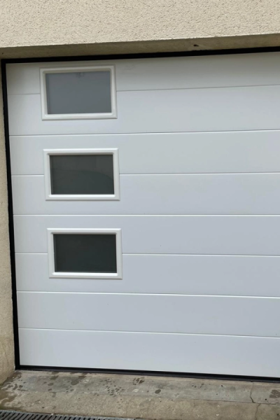 Porte de garage sectionnelle blanche à trois hublots empilés sur mur crépi beige