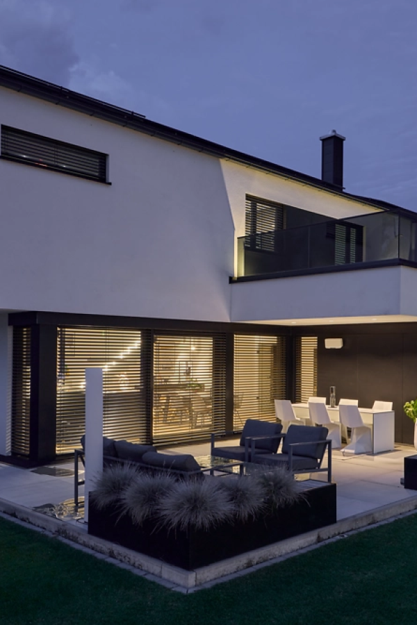 Maison contemporaine blanche au crépuscule, brise-soleil horizontaux et terrasse salon de jardin
