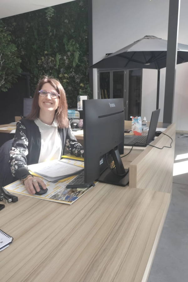 Conseillère souriante à un bureau avec mur végétal et parasol gris en arrière-plan