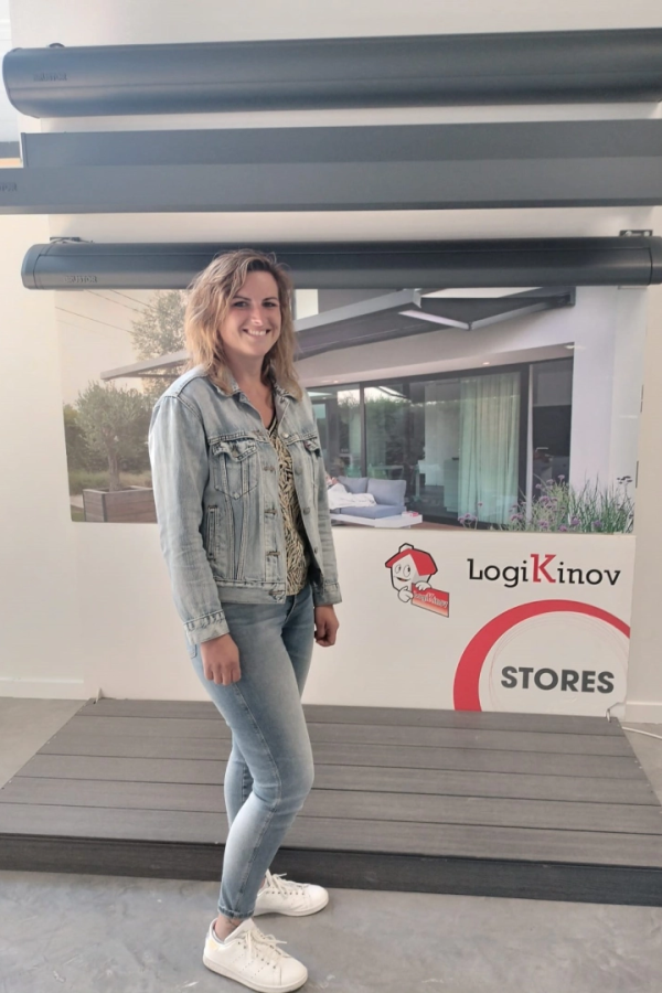 Femme souriante en jean dans un stand d'échantillons de stores avec affiche STORES au mur