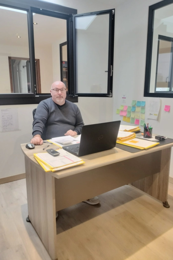 Collaborateur chauve lunettes à bureau, dossiers jaunes et post-it colorés au mur
