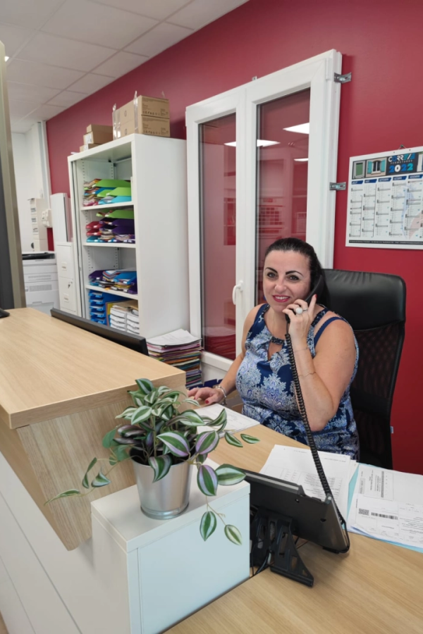 Collaboratrice au téléphone dans bureau rouge, classeurs colorés et plante sur bureau bois