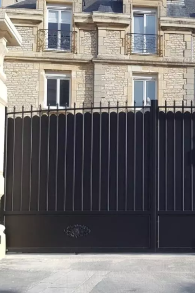 Portail battant noir style traditionnel, rosace basse et barreaudage pointu devant maison pierre