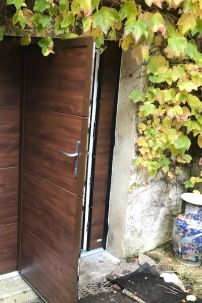 Porte d'entrée aspect bois marron entrouverte sur mur pierre, lierre jaune et vase bleu