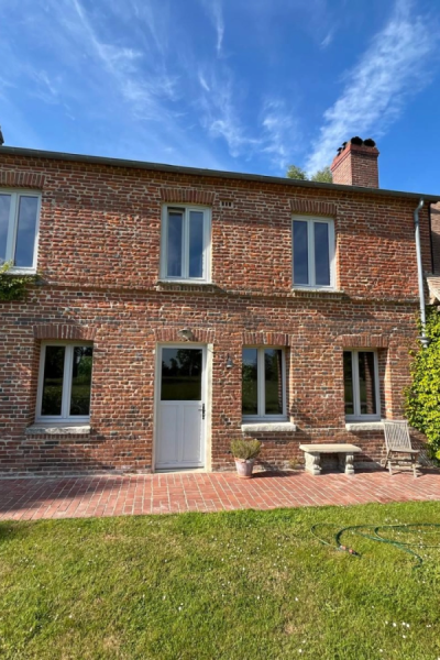 Maison briques rouges avec menuiseries gris clair, terrasse briques et pelouse sous ciel bleu