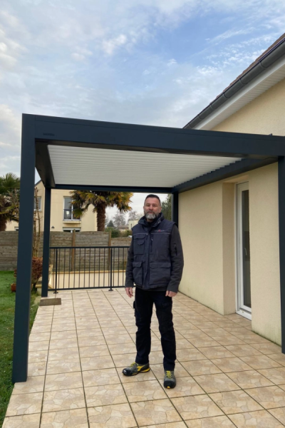 Technicien en gilet gris sous pergola bioclimatique anthracite à lames blanches sur terrasse