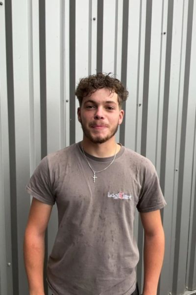 Jeune homme en t-shirt gris tâché avec logo brodé devant bardage métallique ondulé