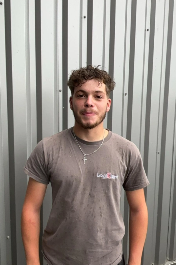 Jeune homme en t-shirt gris tâché avec logo brodé devant bardage métallique ondulé