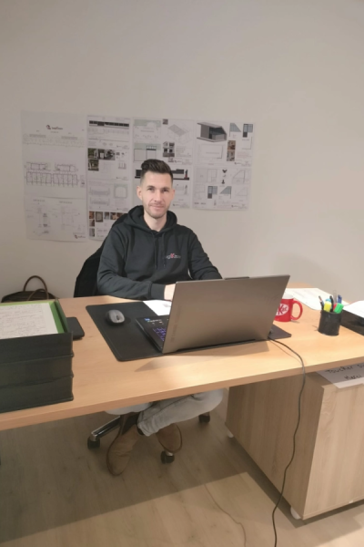Homme en hoodie noir à un bureau avec plans architecturaux affichés au mur