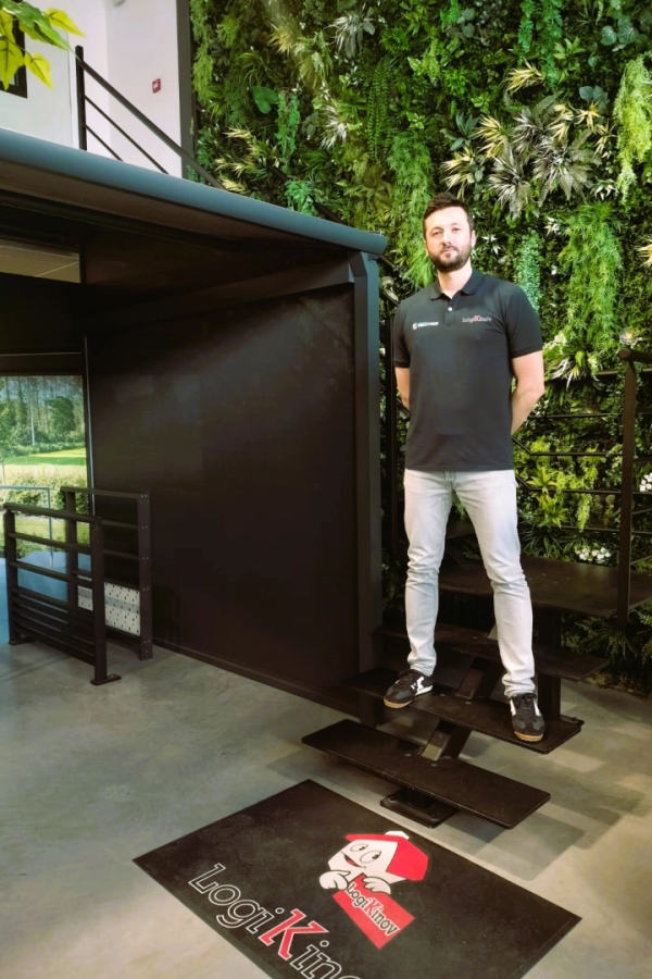 Technicien polo Logikinov sur escalier métal noir, mur végétal et tapis logo au sol