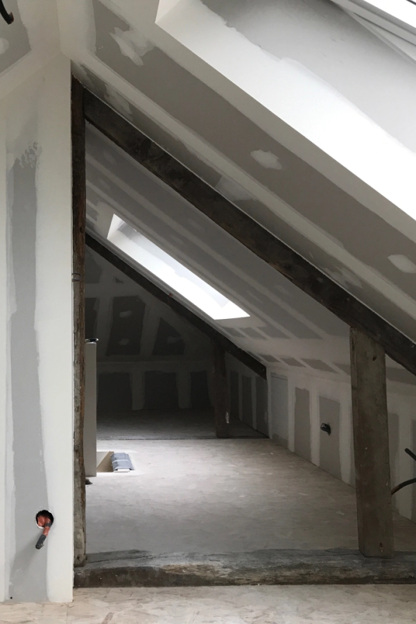Combles en placo blanc avec poutres bois apparentes, velux et sol brut