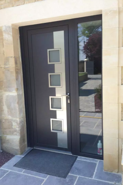 Porte d'entrée anthracite avec bande inox, quatre hublots carrés et imposte vitrée mur pierre