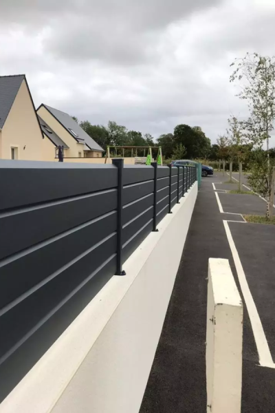 Clôture brise-vue aluminium anthracite à lames horizontales sur muret crème le long d'une route
