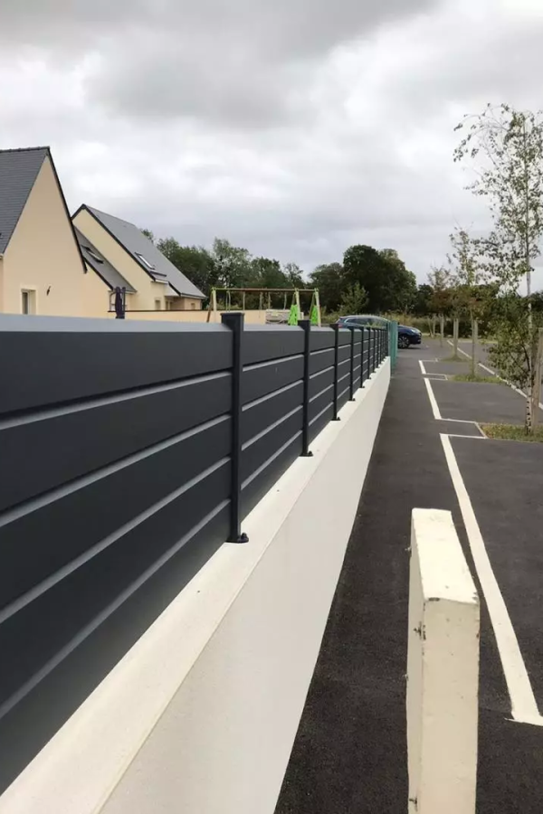 Clôture brise-vue aluminium anthracite à lames horizontales sur muret crème le long d'une route