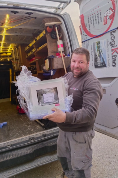 Chef d'équipe souriant tenant un châssis emballé devant utilitaire aménagé et sticker services