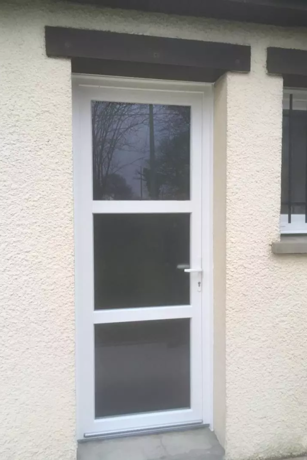 Porte PVC blanche à trois carreaux vitrés sur mur crépi beige, sous linteau bois foncé