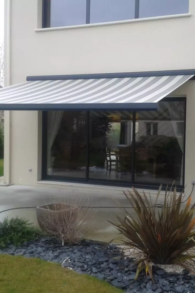 Store banne rayures gris et blanc au-dessus d'une baie vitrée sur façade beige