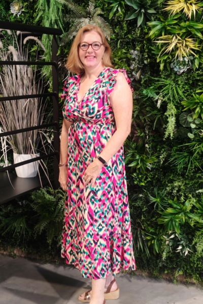 Femme souriante robe colorée devant mur végétal avec étagère métal et graminée décorative