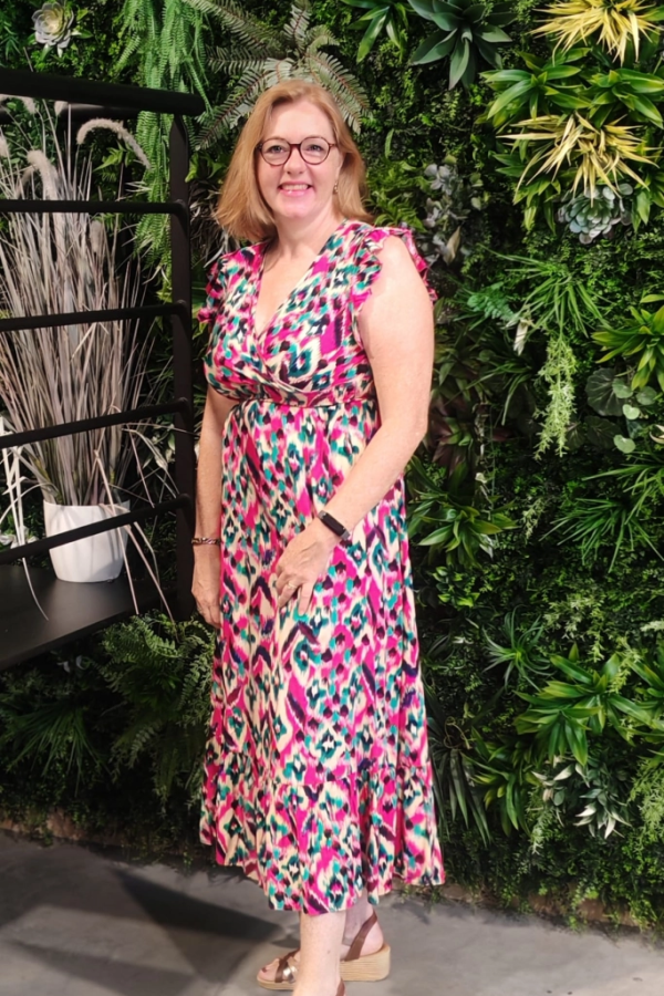 Femme souriante robe colorée devant mur végétal avec étagère métal et graminée décorative