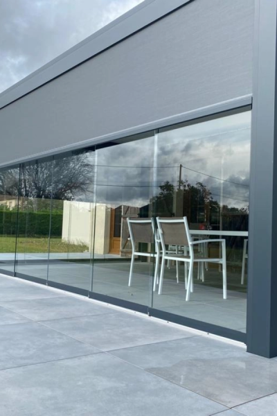 Paroi vitrée coulissante anthracite sur terrasse avec salon blanc et stores intérieurs