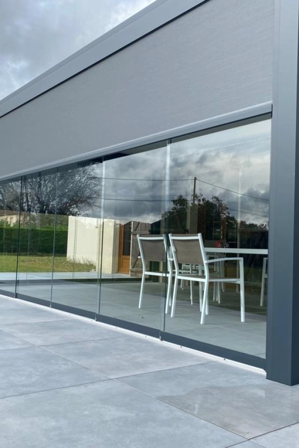 Paroi vitrée coulissante anthracite sur terrasse avec salon blanc et stores intérieurs