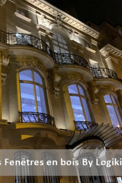 Façade haussmannienne de nuit, fenêtres bois cintrées éclairées et balcons fer forgé