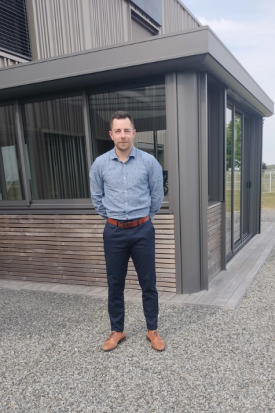 Homme en chemise bleue devant extension anthracite avec grandes baies vitrées et bardage bois