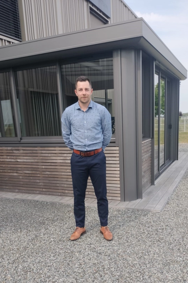 Homme en chemise bleue devant extension anthracite avec grandes baies vitrées et bardage bois