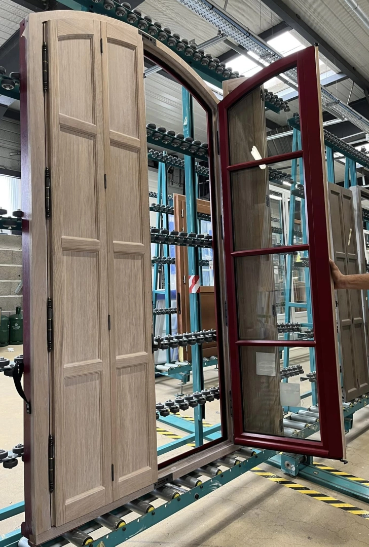 Atelier fenêtre cintrée volet bois clair et vantail rouge bordeaux sur convoyeur bleu