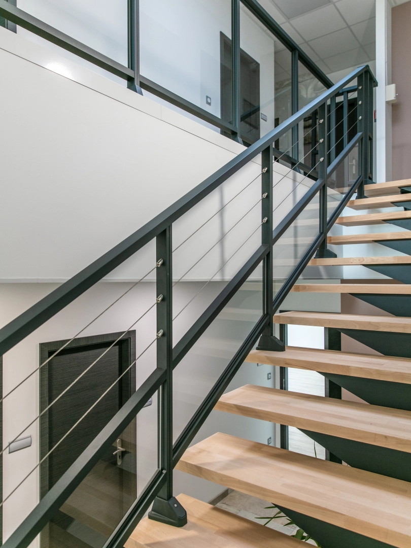 Escalier bois clair, garde-corps câbles inox et rambarde verre noir dans intérieur blanc