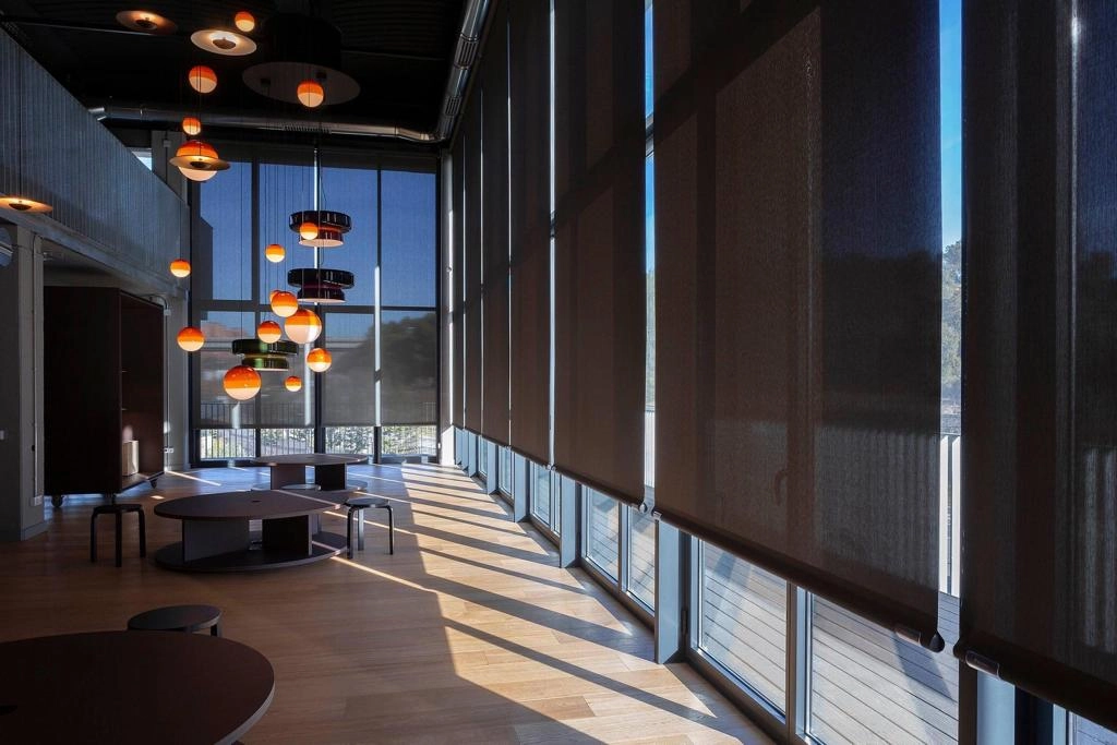 Grandes baies avec stores occultants gris, suspensions orange et tables basses rondes