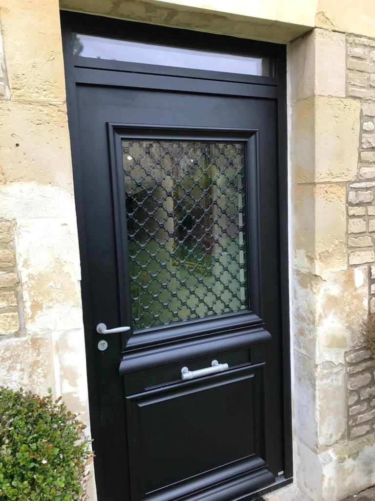 Porte noire classique vitrée à grille trèfles et imposte sur façade pierre claire