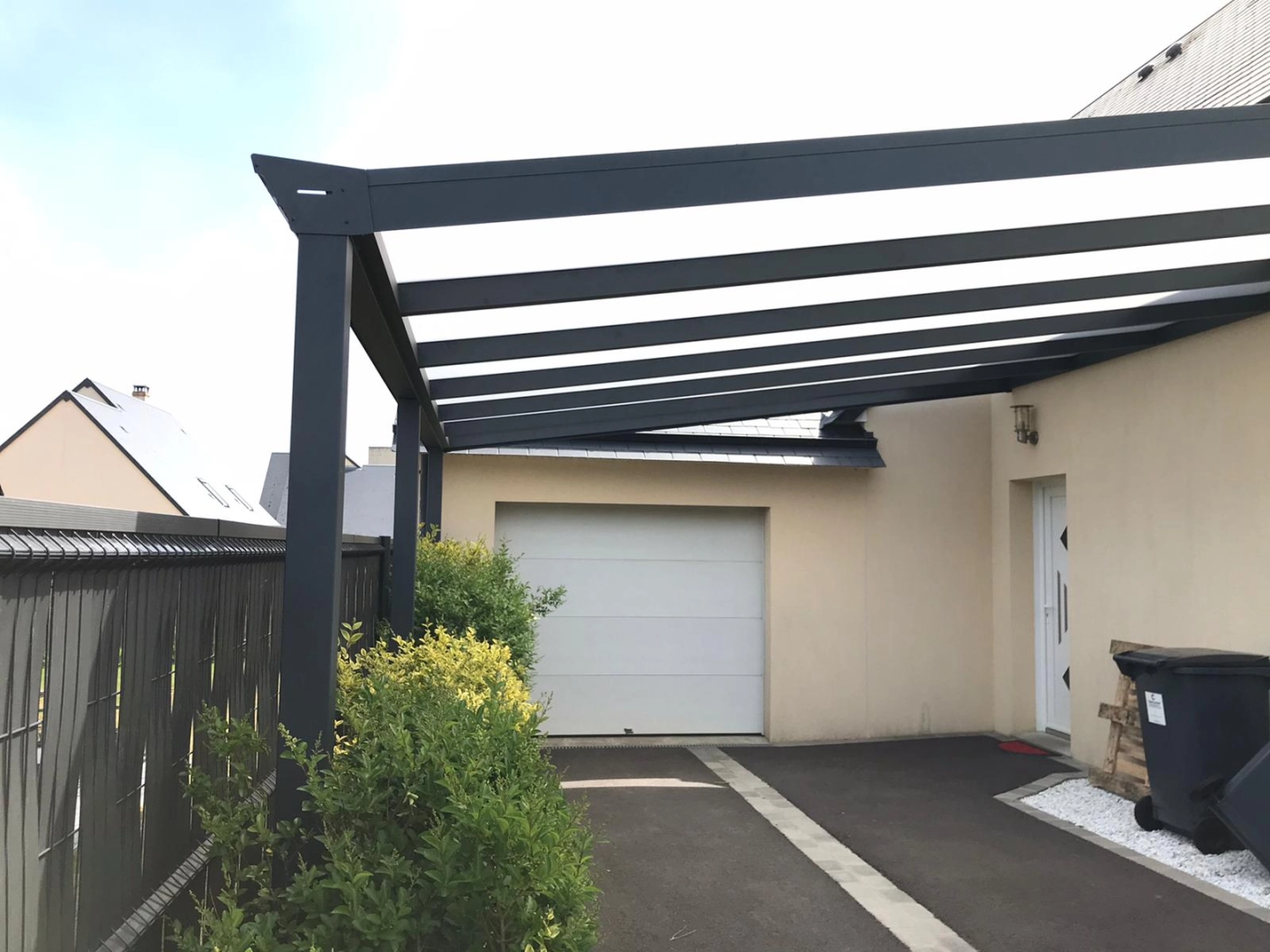 Carport anthracite toiture mixte le long d'allée enrobée devant garage et porte blanche